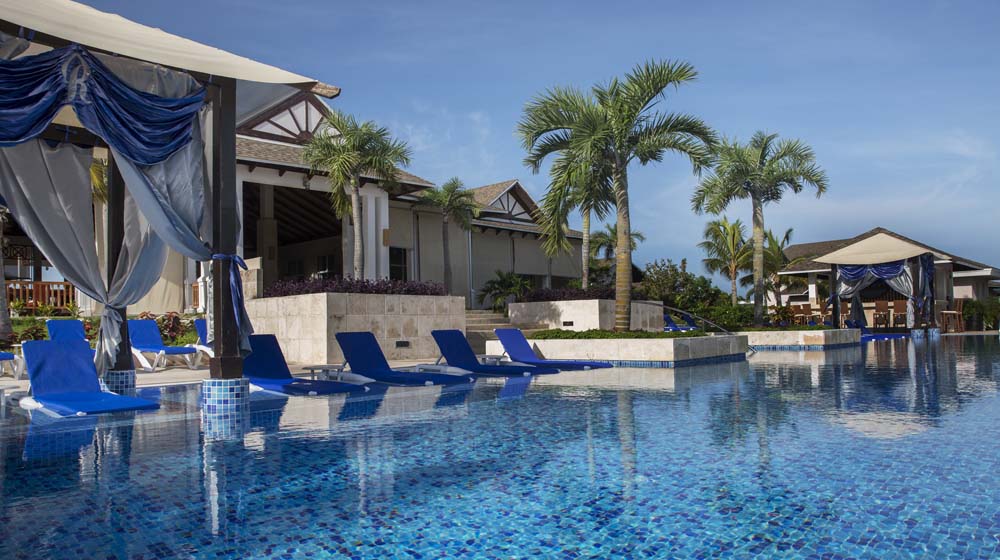 a pool with lounge chairs and umbrellas by a building